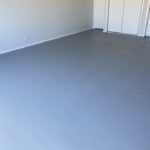An empty indoor room featuring a smooth, freshly applied grey floor coating and white walls.