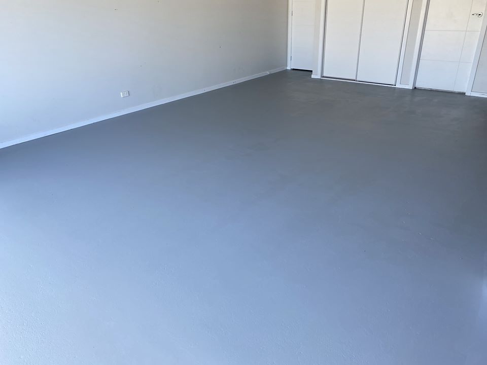 An empty indoor room featuring a smooth, freshly applied grey floor coating and white walls.