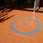 A terracotta-coloured stencilled concrete driveway featuring a large circular pattern with grey accents.