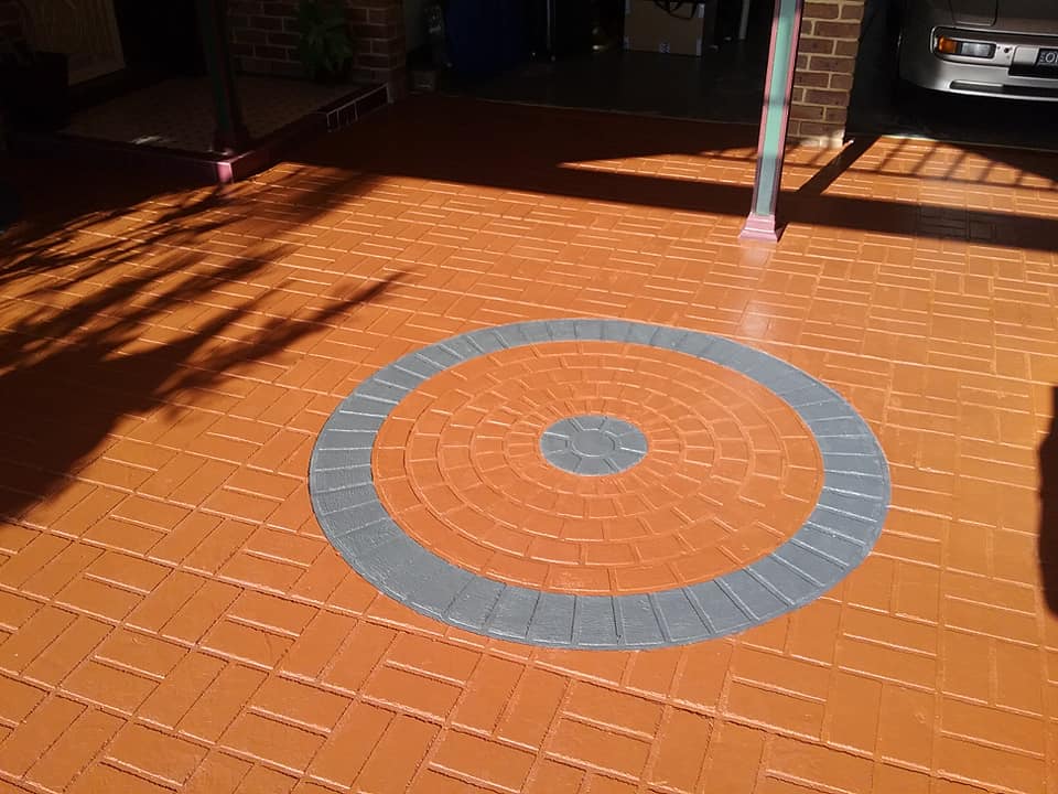 A terracotta-coloured stencilled concrete driveway featuring a large circular pattern with grey accents.