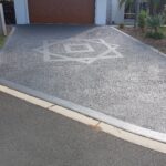 A textured grey driveway with a light grey geometric star-and-square pattern leading to a residential garage door.