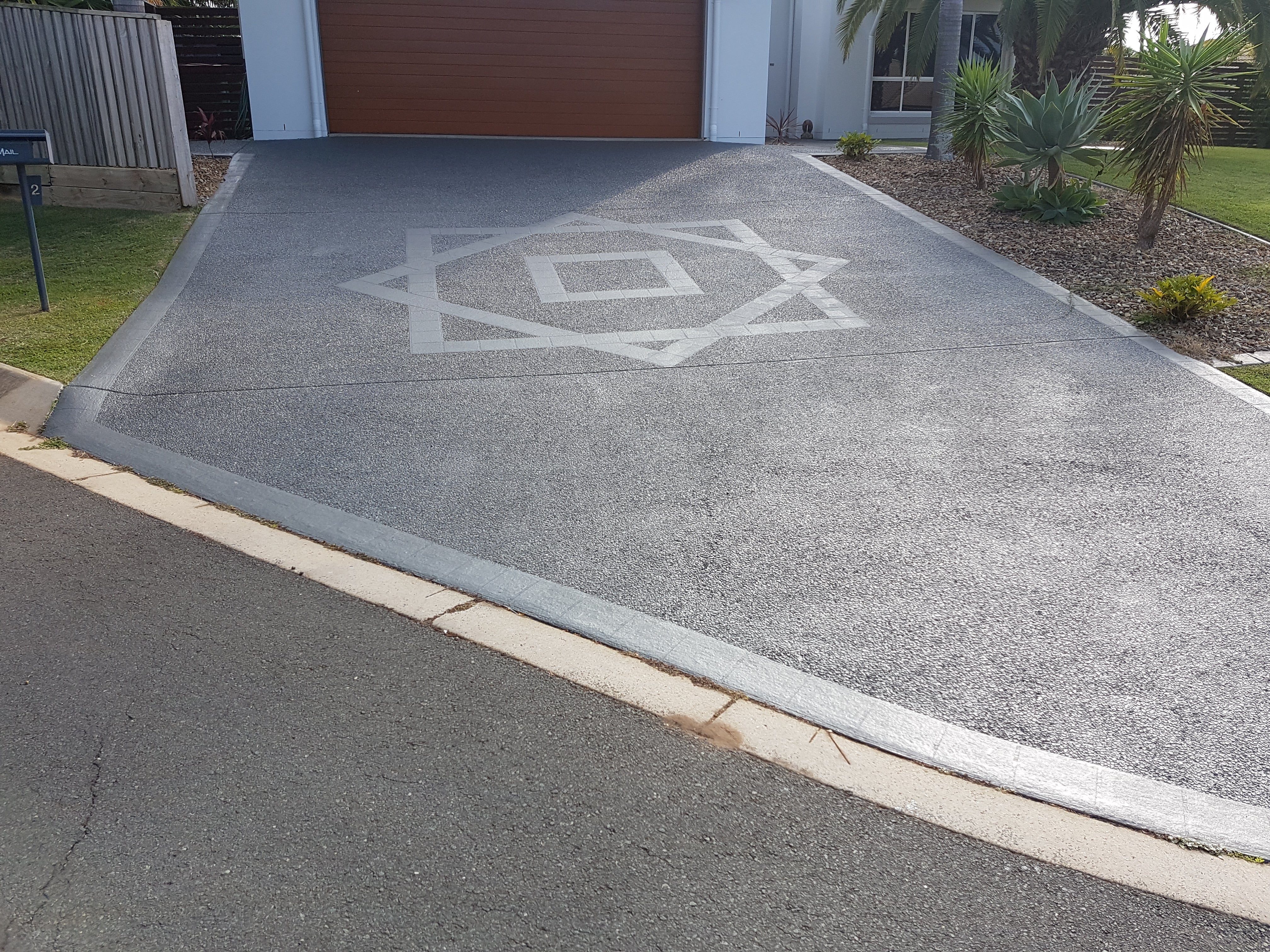 A textured grey driveway with a light grey geometric star-and-square pattern leading to a residential garage door.
