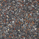 A close-up of dark grey exposed aggregate concrete featuring a dense mix of small black, translucent white, and rusty orange pebbles.