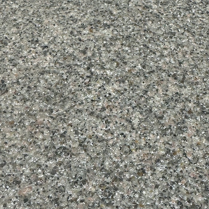 A glossy, textured surface composed of small, tightly packed grey, tan, and white pebbles or stone chips embedded in a clear resin.