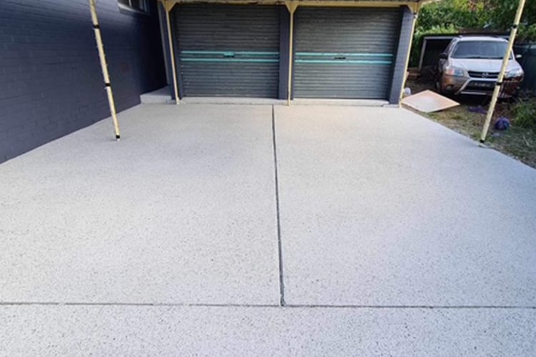 A freshly resurfaced, light-grey speckled driveway in front of a dark grey house with matching dark grey garage doors.