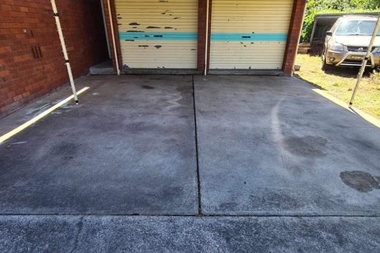 A weathered and stained grey concrete driveway leading to a two-car garage with cream-coloured doors.