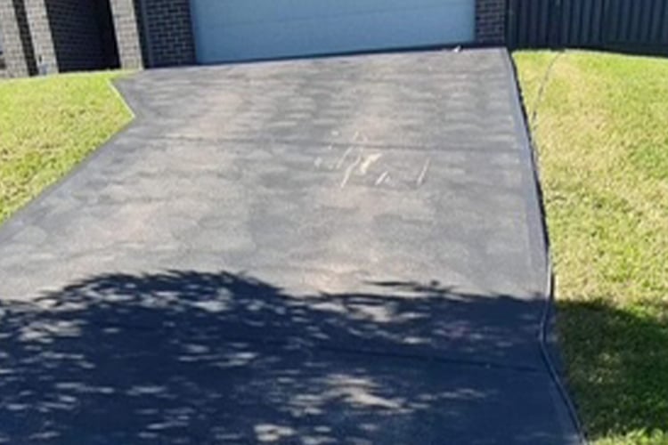 A dark-coloured asphalt or sealed driveway curving slightly between grassy lawns toward a garage.