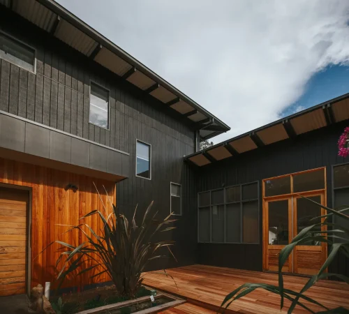 Modern two-storey house with dark charcoal vertical siding, natural wood accents, and a large timber deck.